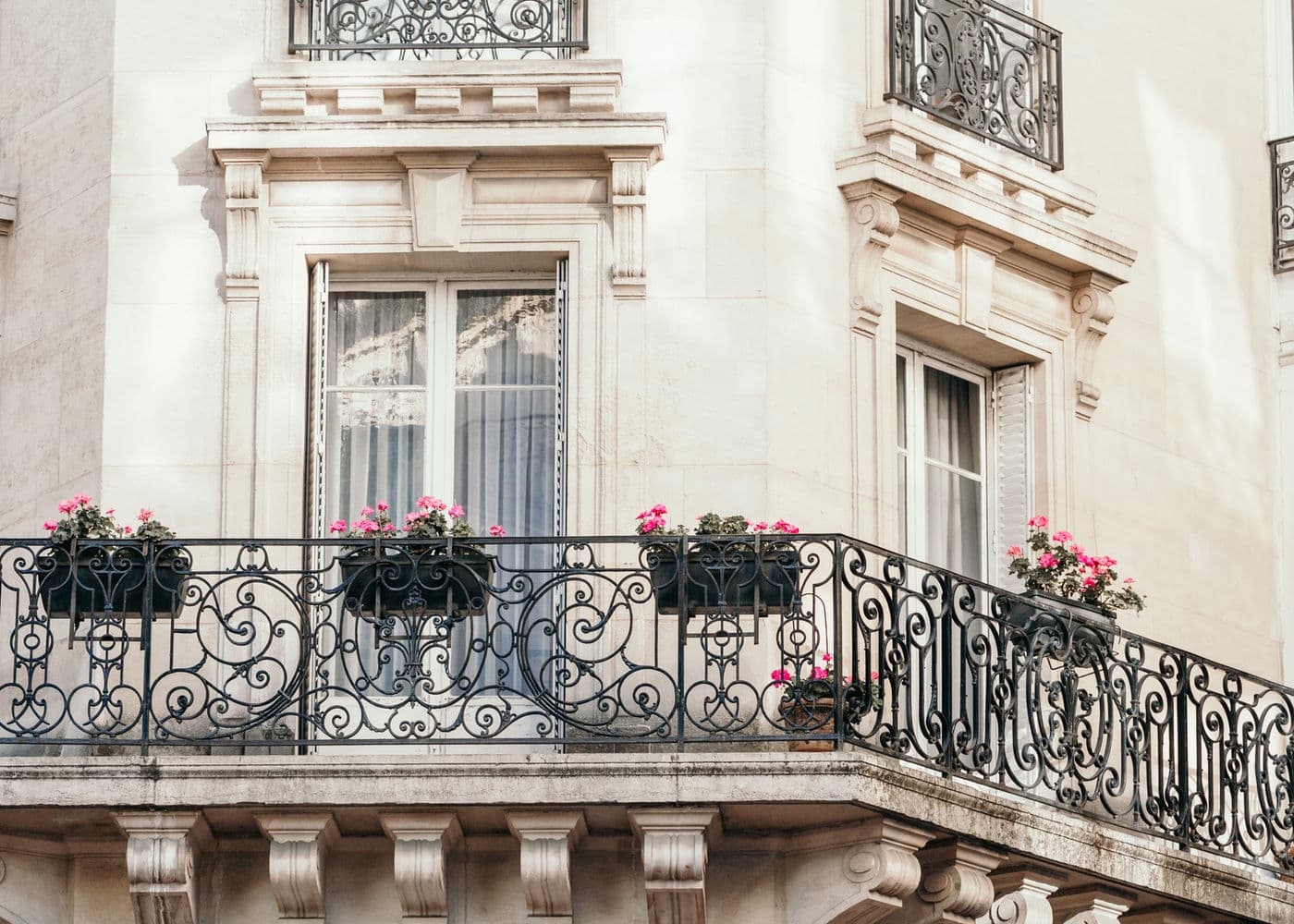 Balcon en fer forgé fleuri de géraniums sur une façade en pierre de taille